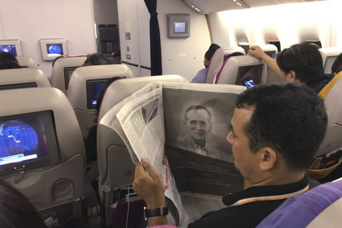 Рейс Thai Airways приземлился в аэропорту Суварнабхуми в Бангкоке 13 октября. Пассажир читает о Его Величестве Пумипоне Адульядете. Фото Чарльз Дхарапак Associated Press
